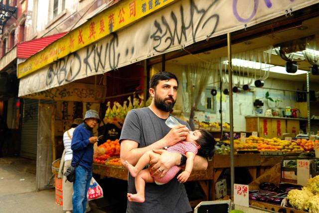 À man feeds a toddler while walking on the street in  Chinatown in the Manhattan borough of New York City on May 10, 2026. (Photo by CHARLY TRIBALLEAU / AFP)