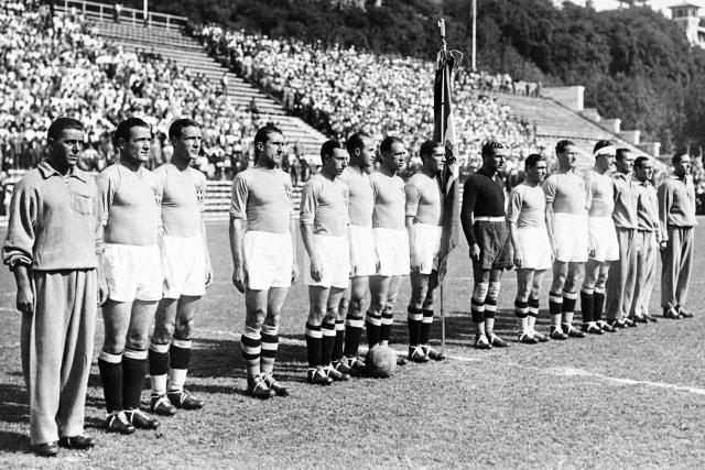 (FILES) Giuseppe Meazza (C) holding the flag and the Italian football team listen to the national anthem before the match of the World Cup's 1934 in Italy. In 1934, the first World Cup in Europe was held in Italy. “May God help him if he fails,” the dictator Benito Mussolini is said to have warned the Italian manager, Vittorio Pozzo. Il Duce wanted propaganda for his regime and knew exactly how to get it: by organising a World Cup... and winning it. (Photo by AFP)