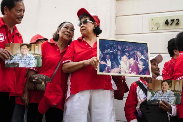Supporters of Thailand's former prime minister Thaksin Shinawatra hold his pictures as they wait outside of his residency in Bangkok on May 11, 2026. Thailand's former prime minister Thaksin Shinawatra was released early from prison on May 11, raising the prospect of a return to the spotlight for the political heavyweight. (Photo by chanakarn LAOSARAKHAM / AFP)