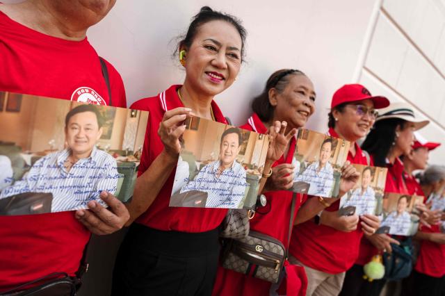 Supporters of Thailand's former prime minister Thaksin Shinawatra hold his pictures as they wait outside of his residency in Bangkok on May 11, 2026. Thailand's former prime minister Thaksin Shinawatra was released early from prison on May 11, raising the prospect of a return to the spotlight for the political heavyweight. (Photo by chanakarn LAOSARAKHAM / AFP)