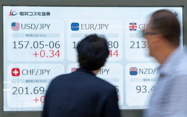 Pedestrians look at an electronic display board showing the exchange rates between the yen and major world currencies including a rate against US dollar (top, L) along a street in Tokyo on May 11, 2026. (Photo by Kazuhiro NOGI / AFP)