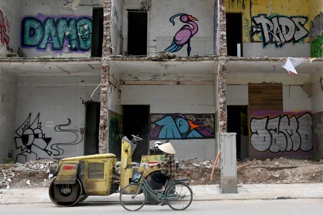 A woman cycles past a demolition site in Hanoi on May 11, 2026. (Photo by Nhac NGUYEN / AFP)