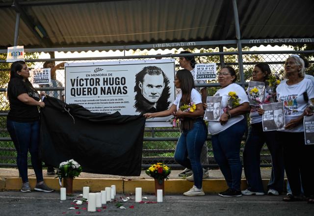 Women uncover a sign in tribute to late Venezuelan political prisoner Victor Hugo Quero Navas during Mother's Day outside El Rodeo I prison in Guatire, Miranda state, Venezuela on May 10, 2026. Venezuelan authorities exhumed the body of Victor Hugo Quero Navas, a political prisoner who died in July 2026 but whose death was not officially acknowledged until May 7, 2026, prompting criticism from civil society and the opposition, an AFP journalist reported. (Photo by Juan BARRETO / AFP)