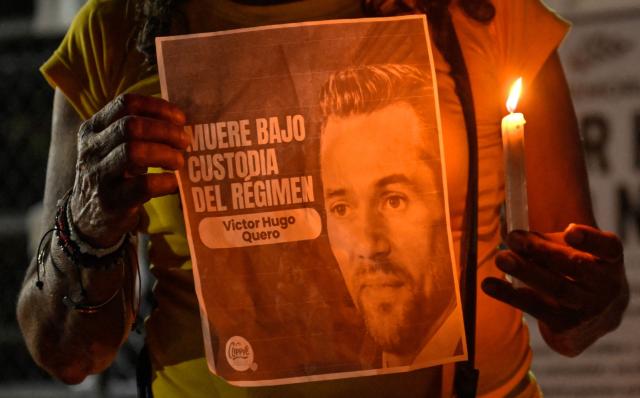 A woman holds a sign depicting late Venezuelan political prisoner Victor Hugo Quero Navas during Mother's Day outside El Rodeo I prison in Guatire, Miranda state, Venezuela on May 10, 2026. Venezuelan authorities exhumed the body of Victor Hugo Quero Navas, a political prisoner who died in July 2025 but whose death was not officially acknowledged until May 7, 2026, prompting criticism from civil society and the opposition, an AFP journalist reported. (Photo by Juan BARRETO / AFP)