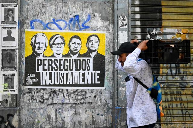 A man walks past a sign tha reads 'unjustly persecuted' featuring Guatemalan journalist and founder of the former newspaper 'El Periodico', Jose Ruben Zamora (L), Guatemalan former lawyer of the International Commission against Impunity in Guatemala (CICIG), Claudia Gonzalez (2nd L) and Maya leaders Luis Pacheco and Hector Chaclan in a street of Guatemala City on May 12, 2026. (Photo by Johan ORDONEZ / AFP)