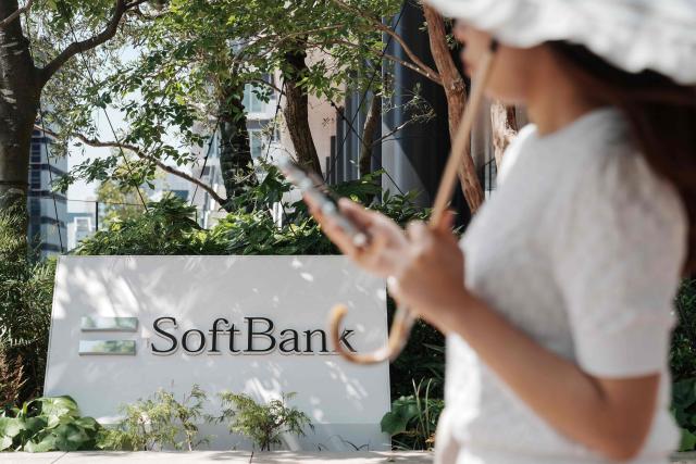 A woman walks past the logo of SoftBank Group Corp. displayed at the company's headquarters in Tokyo on May 13, 2026. (Photo by Kazuhiro NOGI / AFP)