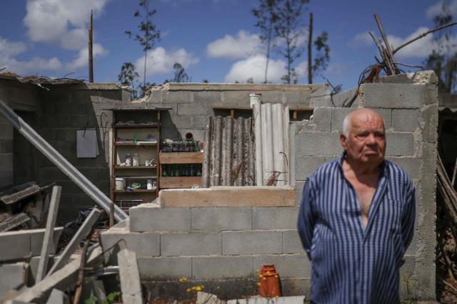 Manuel Calhanas, a 79-year-old retiree, poses for a photo in the backyard of his house located in the middle of a eucalyptus and pine trees forest at Marinha Grande, central Portugal, on May 7, 2026. In a forest in central Portugal, the whirring of chainsaws sets the pace for the teams working to clear paths blocked by thousands of trees felled during the storms earlier this year, in a race against time as fire season approaches. Using heavy machinery, forestry workers and military personnel coordinate to push the felled trunks to the sides of the paths to reopen access to the Marinha Grande forest, which is essential for the rapid intervention of emergency services. (Photo by PATRICIA DE MELO MOREIRA / AFP) / TO GO WITH STORY BY LEVI FERNANDES