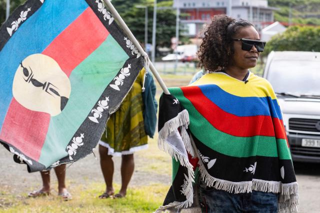 A pro-independence activist waves a flag during a demonstration to mark the second anniversary of the spring 2024 riots in Noumea, in the French overseas collectivity of New Caledonia, on May 13, 2026. Two years after the violence that left 14 dead and caused several billion euros’ worth of damage in New Caledonia, tensions and mistrust remain, as the debate over the electoral roll, which sparked the insurrectional crisis, is still unresolved. (Photo by Delphine MAYEUR / AFP)