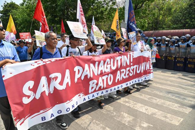 Protesters carrying a banner reading "Sara (Philippine Vice President Sara Duterte) take responsibility, arrest Bato" (the nickname of Senator Ronald dela Rosa) walk past a column of anti-riot policemen as they march towards the Senate in Manila on May 13, 2026. Former Philippine leader Rodrigo Duterte's top drug war enforcer said he would never surrender to an international court, while pleading for current President Ferdinand Marcos to intervene on his behalf. (Photo by TED ALJIBE / AFP)