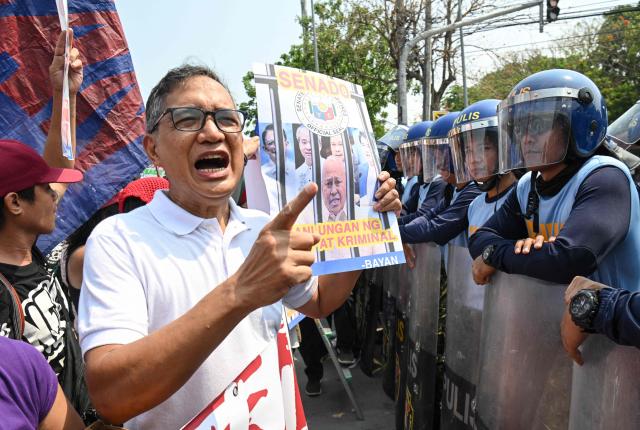 Former Philippines' legislator Teddy Casino (L) speaks to anti-riot policemen while holding a placard with a portrait of Senator Ronald dela Rosa during a protest in front of the Senate in Manila on May 13, 2026. Former Philippine leader Rodrigo Duterte's top drug war enforcer said he would never surrender to an international court, while pleading for current President Ferdinand Marcos to intervene on his behalf. (Photo by TED ALJIBE / AFP)