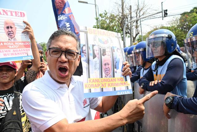 Former Philippines' legislator Teddy Casino (L) speaks to anti-riot policemen while holding a placard with a portrait of Senator Ronald dela Rosa during a protest in front of the Senate in Manila on May 13, 2026. Former Philippine leader Rodrigo Duterte's top drug war enforcer said he would never surrender to an international court, while pleading for current President Ferdinand Marcos to intervene on his behalf. (Photo by TED ALJIBE / AFP)