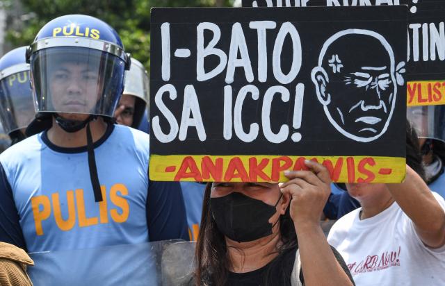 A protester holds a placard reading "throw (refering to Senator "Bato" Ronald dela Rosa) to the International Criminal Court (ICC)" next to policemen during a protest in front of the Senate in Manila on May 13, 2026. Former Philippine leader Rodrigo Duterte's top drug war enforcer said he would never surrender to an international court, while pleading for current President Ferdinand Marcos to intervene on his behalf. (Photo by TED ALJIBE / AFP)