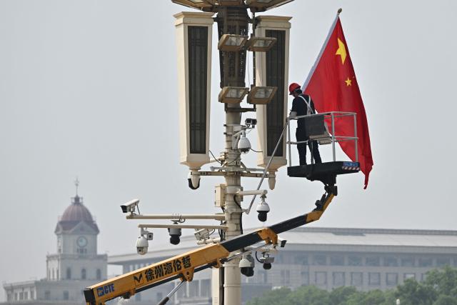 A worker removes a Chinese flag from Tiananmen Square in Beijing on May 13, 2026, ahead of a visit by US President Donald Trump. (Photo by Pedro PARDO / AFP)
