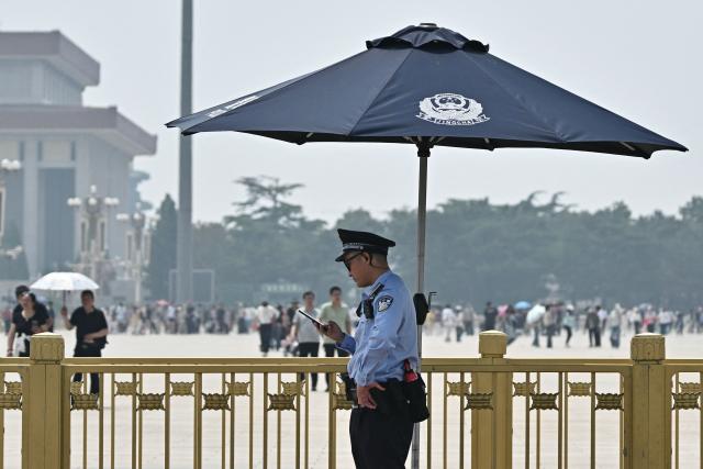 A police officer checks his phone on Tiananmen Square in Beijing on May 13, 2026, ahead of a visit by US President Donald Trump. (Photo by Pedro PARDO / AFP)