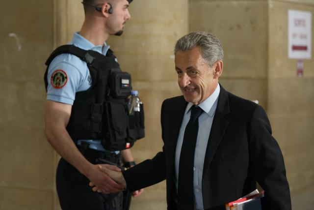 France's former president Nicolas Sarkozy shakes hands with a police officer as he arrives for his appeal trial over charges he had sought Libyan financing for his 2007 election in exchange for helping improve Tripoli's image after deadly bombing, at the Palais de Justice courthouse in Paris on May 13, 2026. Nearly two months after the start of the appeal trial regarding allegations of Libyan funding of Nicolas Sarkozy's 2007 presidential campaign, the public prosecutor's office is due to announce on May 13, 2026, the sentences it is seeking against Nicolas Sarkozy and his nine co-defendants, in this case that has already seen the former head of state serve time in prison. (Photo by Alain JOCARD / AFP)