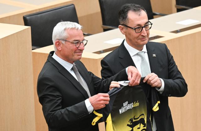 Cem Oezdemir (R) of the Greens holds a jersey in the colors of his federal state he was given by Thomas Strobl (L), new president of Baden Wuerttemberg's regional parliament, after Oezdemir was elected as the new State Premier of Baden-Wuerttemberg at the parliament's plenary hall in Stuttgart, southern Germany, on May 13, 2026. The inaugural session of the new state parliament of Baden-Wuerttemberg took place the day before, on May 12, 2026, following state elections on March 8, 2026. (Photo by THOMAS KIENZLE / AFP)