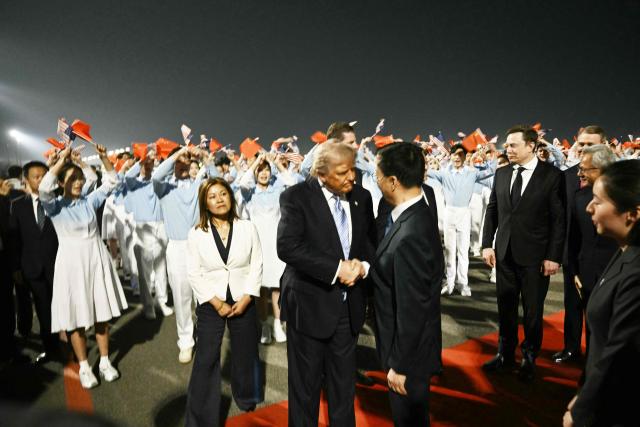 US President Donald Trump (C) is greeted by China’s Vice President Han Zheng as SpaceX, Twitter and electric car maker Tesla CEO Elon Musk (R) looks on at Beijing Capital Airport in Beijing on May 13, 2026. (Photo by Brendan SMIALOWSKI / AFP)
