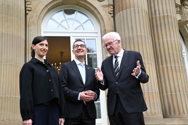 Baden-Wuerttemberg's new State Premier Cem Oezdemir (C) of the Greens, his wife Flavia Zaka (L) and his predecessor Winfried Kretschmann stand on the terrace of Villa Reitzenstein in Stuttgart, southern Germany, after Oezdemir took over the post, on May 13, 2026.  (Photo by Bernd Weißbrod / POOL / AFP)