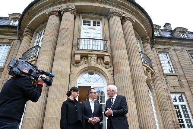 Baden-Wuerttemberg's new State Premier Cem Oezdemir (C) of the Greens, his wife Flavia Zaka (L) and his predecessor Winfried Kretschmann stand on the terrace of Villa Reitzenstein in Stuttgart, southern Germany, after Oezdemir took over the post, on May 13, 2026.  (Photo by Bernd Weißbrod / POOL / AFP)