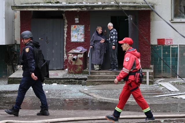 Local residents stand on the porch of a damaged residential building as a Ukrainian rescuer and medic walk by following an air attack in Odesa on May 13, 2026, amid the Russian invasion in Ukraine. (Photo by Oleksandr GIMANOV / AFP)