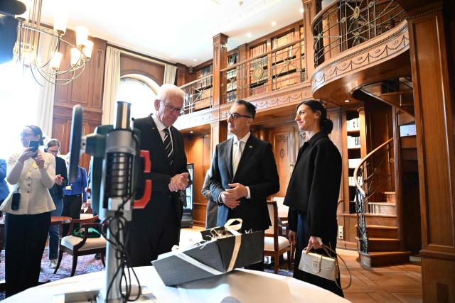Baden-Wuerttemberg's new State Premier Cem Oezdemir (C) of the Greens, his wife Flavia Zaka (R) and his predecessor Winfried Kretschmann echchange presents in the library of Villa Reitzenstein in Stuttgart, southern Germany, after Oezdemir took over the post, on May 13, 2026.  (Photo by Bernd Weißbrod / POOL / AFP)