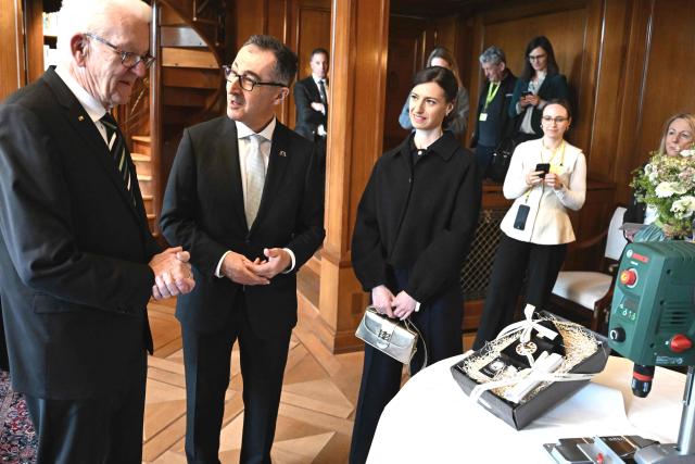 Baden-Wuerttemberg's new State Premier Cem Oezdemir (2nd L) of the Greens, his wife Flavia Zaka (3rd L) and his predecessor Winfried Kretschmann (L) echchange presents in the library of Villa Reitzenstein in Stuttgart, southern Germany, after Oezdemir took over the post, on May 13, 2026.  (Photo by Bernd Weißbrod / POOL / AFP)