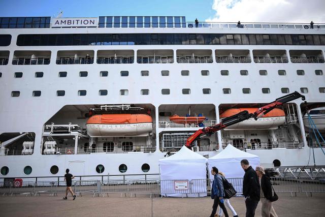 Passers-by walk past the Bahamas-registered cruise ship Ambition after passengers were confined following the outbreak of a gastrointestinal illness onboard, at the Bordeaux port in Bordeaux, southwestern France on May 13, 2026. French authorities on May 13 confined more than 1,700 passengers and crew on a British cruise ship docked in Bordeaux after an elderly passenger died, said officials, who played down any links to the hantavirus scare. (Photo by Christophe ARCHAMBAULT / AFP)