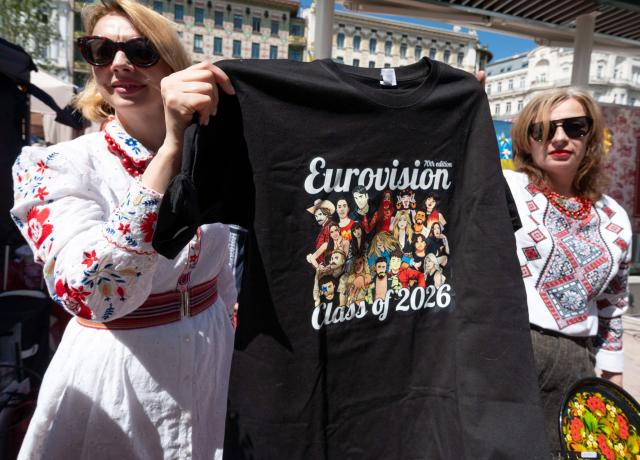 Ukrainian women, dressed in traditional costumes, hold up a T-shirt with the ESC competitors, during the ESC side event 'Eurovision Market Contest' at Vienna's Naschmarkt, Austria, where several food and souvenir stalls from different ESC participating countries take part, on May 13, 2026. (Photo by Joe KLAMAR / AFP)