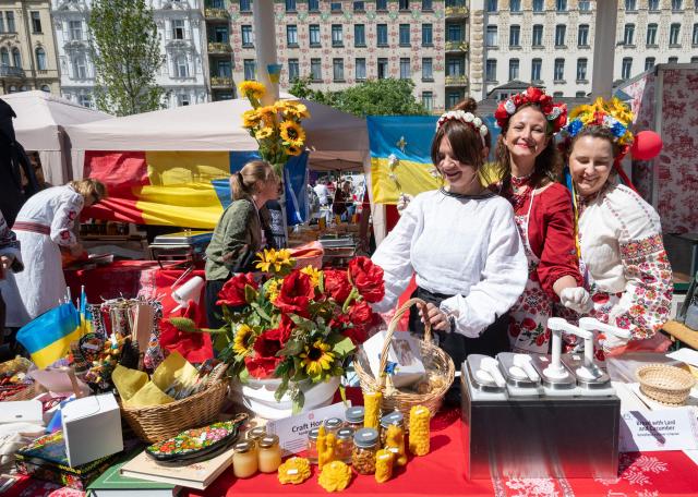 Ukrainian women, dressed in traditional costumes, react during the ESC side event 'Eurovision Market Contest' at Vienna’s Naschmarkt, Austria, where several food and souvenir stalls from different ESC participating countries take part, on May 13, 2026. (Photo by Joe Klamar / AFP)