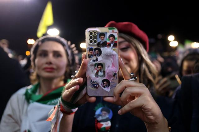 A woman with her mobile phone containing photos of Iran's current supreme leader Ayatollah Mojtaba Khamenei and his predecessor and late father Ayatollah Ali Khamenei, takes pictures of the farewell ceremony of Iran's national football team ahead of their departure for the 2026 FIFA World Cup, in Tehran on May 13, 2026. The president of the Iranian Football Federation said late May 9 that if Iran dropped out of the World Cup, it would deprive the country of a "major diplomatic asset". World football's governing body FIFA has insisted for weeks that Iran will take part. Iran, who are due to be based in Tucson, Arizona, during the World Cup, face New Zealand, Belgium and Egypt in Group G. The Iranians open their World Cup campaign against New Zealand in Los Angeles on June 15. (Photo by ATTA KENARE / AFP) / 