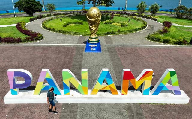 This aerial view shows a man walking past a giant replica of the FIFA World Cup trophy and a city sign at the Cinta Costera in Panama City on May 13, 2026. Panama will play in the FIFA World Cup hosted by the United States, Mexico, and Canada from June 11 to July 19, 2026. (Photo by Martin BERNETTI / AFP)