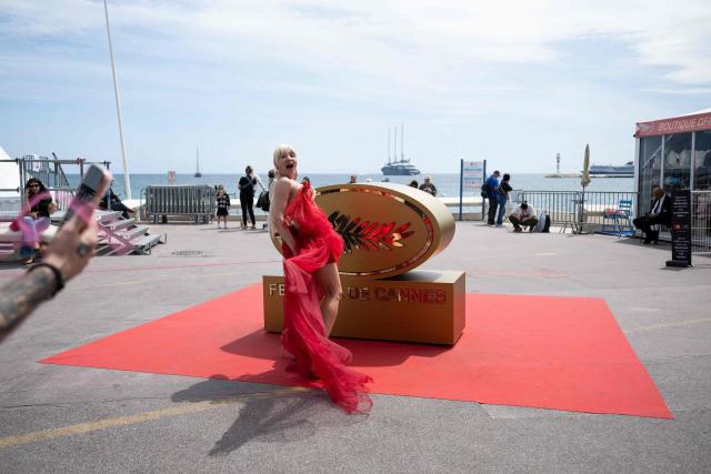 A woman in evening attire poses in front of the official logo of the Cannes film festival on the Boulevard de la Croisette on the sidelines of the 79th edition of the Cannes Film Festival in Cannes, southern France, on May 13, 2026. (Photo by Anna KURTH / AFP)