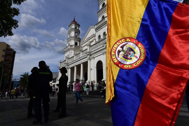 A Colombian flag is pictured next to police officers standing guard ahead of a campaign rally of Colombia's right-wing Presidential candidate Abelardo de la Espriella, from the Defensores de la Patria movement, in Envigado, Colombia on May 13, 2026. Colombia will hold presidential elections on May 31. (Photo by Jaime SALDARRIAGA / AFP)