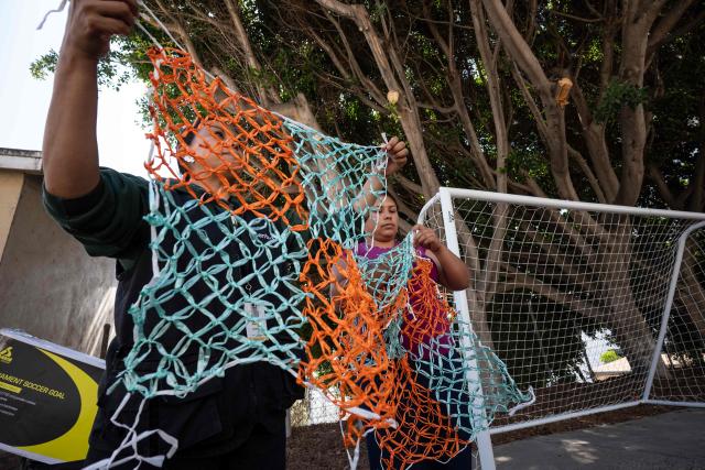 Migrants and advocates work on a football goal net as they rehearse the setup of Tejiendo Redes (Weaving Nets), an art project at Centro 32, a migrants support NGO, ahead of its presentation in Tijuana, Baja California, Mexico, on May 13, 2026. Conceived by Mexican artist Betsabee Romero, the project seeks to give visibility to migrants through art, using the FIFA World Cup as a platform. Finished goals with nets, all woven by migrants in Tijuana, Mexico, will be exhibited at the Mexico-US border before crossing into the United States. (Photo by Guillermo Arias / AFP)