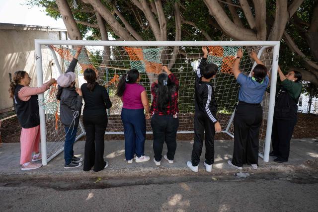 Migrants and advocates work on a football goal net as they rehearse the setup of Tejiendo Redes (Weaving Nets), an art project at Centro 32, a migrants support NGO, ahead of its presentation in Tijuana, Baja California, Mexico, on May 13, 2026. Conceived by Mexican artist Betsabee Romero, the project seeks to give visibility to migrants through art, using the FIFA World Cup as a platform. Finished goals with nets, all woven by migrants in Tijuana, Mexico, will be exhibited at the Mexico-US border before crossing into the United States. (Photo by Guillermo Arias / AFP)