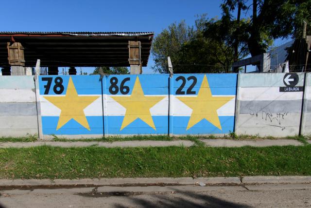 A mural depicting Argentina's World Cup titles in 1978, 1986 and 2022 is seen in the childhood neighborhood of Argentine footballer Lionel Messi in Rosario, Santa Fe province, Argentina, on April 30, 2026. At the age of 12, Lionel Messi ended the career of his first coach. When Enrique Dominguez stopped coaching him in 1999 at the youth club Malvinas Argentinas in the city of Rosario, he resigned, saying he had "already coached the best player in the world", who could now be set to play in his sixth World Cup. (Photo by Marcelo Manera / AFP)