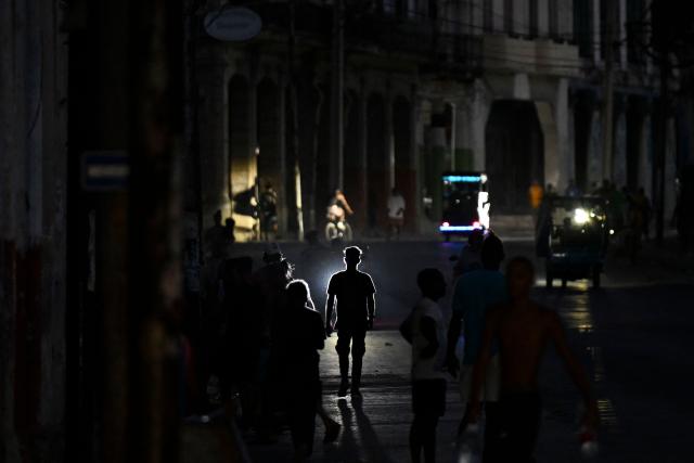 People walk on a street during a blackout in Havana on May 13, 2026. Cuba blamed the United States for the "particularly tense" situation in its power grid on May 13, 2026, which has been plagued by prolonged blackouts, while Washington once again offered $100 million in aid to the island. (Photo by Yamil LAGE / AFP)
