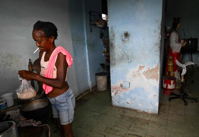 A woman cooks rice while holding a cigarette in her mouth during a blackout in Havana on May 13, 2026. Cuba blamed the United States for the "particularly tense" situation in its power grid on May 13, 2026, which has been plagued by prolonged blackouts, while Washington once again offered $100 million in aid to the island. (Photo by Yamil LAGE / AFP)
