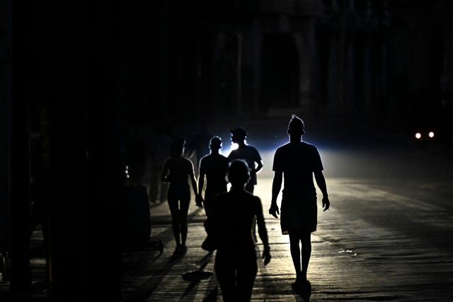 People walk on a street during a blackout in Havana on May 13, 2026. Cuba blamed the United States for the "particularly tense" situation in its power grid on May 13, 2026, which has been plagued by prolonged blackouts, while Washington once again offered $100 million in aid to the island. (Photo by Yamil LAGE / AFP)