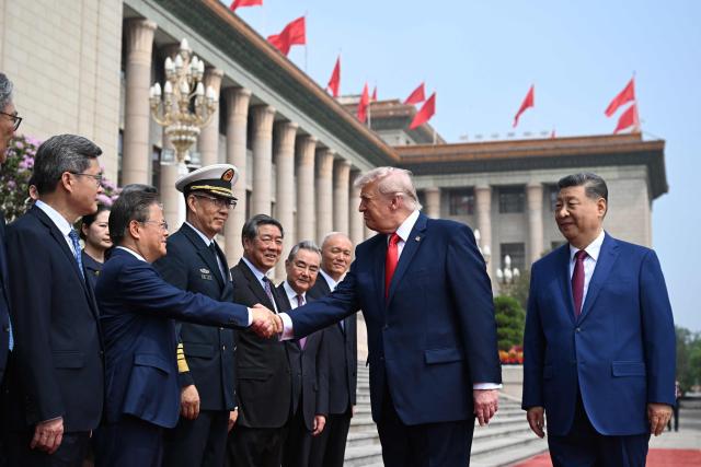US President Donald Trump (C) shakes hands with Zheng Shanjie, Chairman of China's National Development and Reform Commission, as China's President Xi Jinping (R) looks on at the Great Hall of the People in Beijing on May 14, 2026. (Photo by Kenny HOLSTON / POOL / AFP)