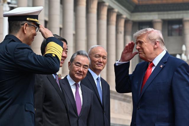 US President Donald Trump (R) salutes China's Defence Minister Dong Jun (L) during a welcome ceremony at the Great Hall of the People in Beijing on May 14, 2026. (Photo by Kenny HOLSTON / POOL / AFP)