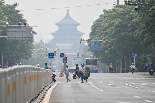 Pedestrians and motorists are seen on a street in Beijing on May 14, 2026, amid a state visit by US President Donald Trump. (Photo by Hector RETAMAL / AFP)