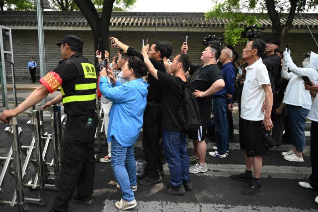 People gather to watch US President Donald Trump's motorcade pass by in Beijing on May 14, 2026. (Photo by GREG BAKER / AFP)
