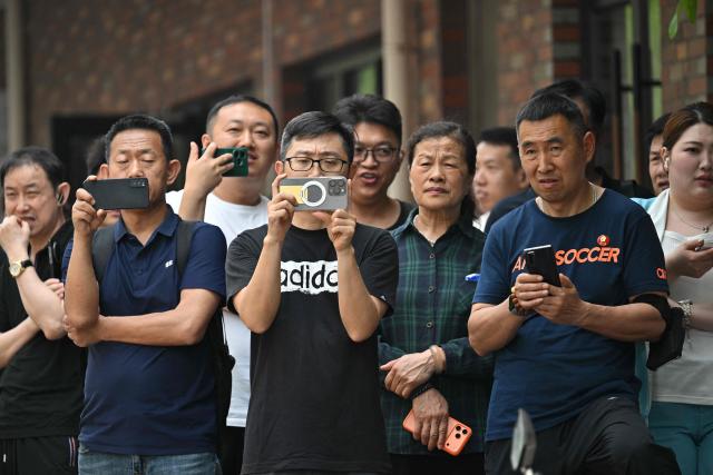 People gather to watch US President Donald Trump's motorcade pass by in Beijing on May 14, 2026. (Photo by HECTOR RETAMAL / AFP)