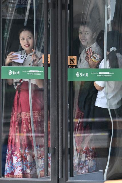Women in a mall try to watch US President Donald Trump's motorcade pass by in Beijing on May 14, 2026. (Photo by HECTOR RETAMAL / AFP)