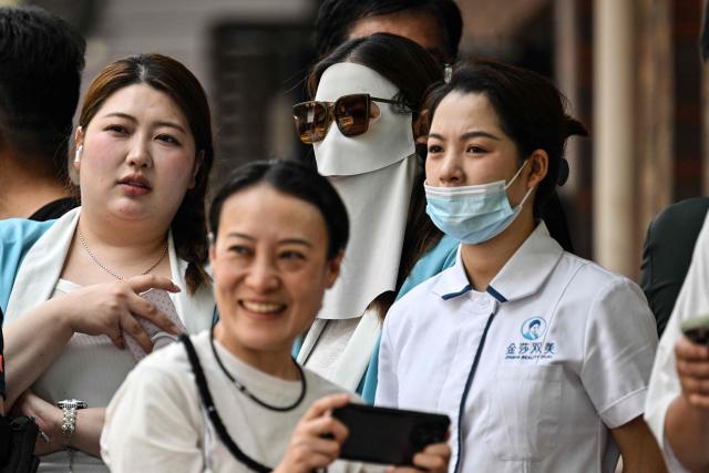 People gather to watch US President Donald Trump's motorcade pass by in Beijing on May 14, 2026. (Photo by HECTOR RETAMAL / AFP)