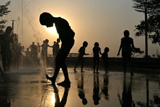 Children are silhouetted as they play in a water fountain at the Sabarmati Riverfront in Ahmedabad on May 13, 2026. (Photo by Shammi MEHRA / AFP)