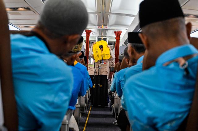 Prospective Indonesian hajj pilgrims learn how to use life jackets from cabin crew aboard a retired Boeing 717 during a pre-departure safety training session at the hajj embarkation centre in Banda Aceh on May 14, 2026. (Photo by CHAIDEER MAHYUDDIN / AFP)