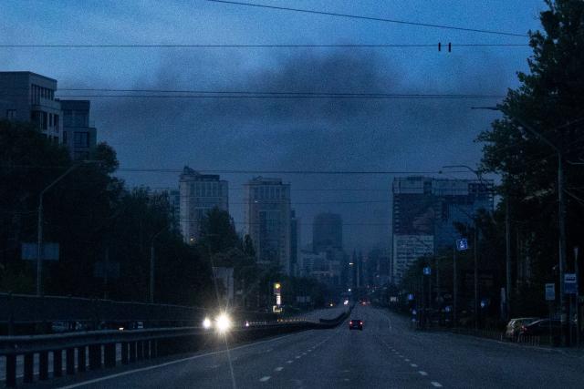 Vehicles are driven along a road as smoke rises above buildings in the background following an air attack in Kyiv on May 14, 2026, amid the Russian invasion of Ukraine. Large-scale Russian strikes on Kyiv killed one person and wounded at least 31 others, city authorities said on May 14, 2026, as Moscow ramped up attacks on Ukraine following a short-lived ceasefire. (Photo by Serhii Okunev / AFP)