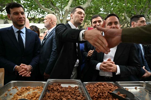 French far-right party Rassemblement National (RN) president Jordan Bardella (C) shakes hands with a vendor next to mayor of Beaucaire Nelson Chaudon (L) during a visit in Beaucaire, southern France on May 14, 2026. (Photo by Gabriel BOUYS / AFP)